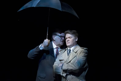 Johnson, in business suit and holding an umbrella, speaks into the ear of Kennedy, wearing a gray overcoat