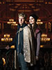 Promo photo by Lauren Parker of Benjamin Reed and Zoe Speas in regalia standing in the balcony of the chandaleir-lit Blackfriars Playhouse.