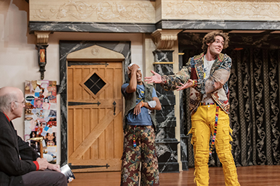 ASC-Romeo_and_Juiliet_2025-4 Benvolio has his hand to his white-capped head in embarrassment at Romeo's insult to an audience member sitting on the stage, Romeo's hands pointing in the patron's direction as he looks forward at the rest of theater audience with a teasing expression on his face.