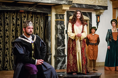 Production photo by Marek K. Photography of Hermione on a black marble like platform looking at Leontes, back to her, while the court watches in the background.