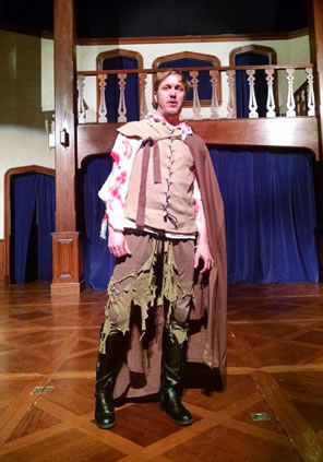 Shakespeare in Elizabethan tunic and kneepants, which are n tatters, blood on his shirt sleeves, cape and black boots