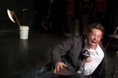 Richard, with crooked left arm and gloved hand, lies on the floor as he shouts a line or laughs, a halberd in a white bucket in the background.