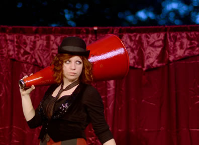 Puck as carnival barker carrying a megaphone on her shoulder
