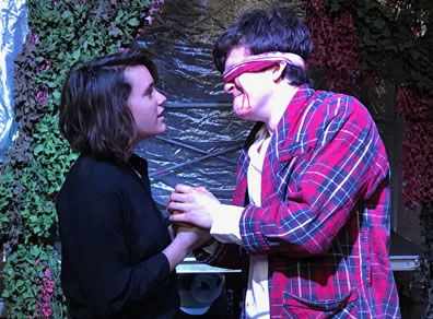 Edgar as Poor Tom in a black shirt with both hands holds the hands of Gloucester in tartan robe and white shirt and a bloody bandage around his eyes with streams of blood down his cheeks and chin.