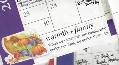 A scattering of pocket calendars, opened to various months, featuring scribbled entries, and a message at the bottom of one page: "Warmth + Family. When we remember the poeple who enrich our lives, we enrich theirs, too."