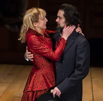 Kate in a lovely red dress lovingly clasps Petruchio after he asks her to "Kiss me Kate."
