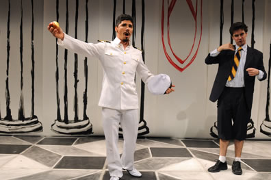 Don Armado in white naval uniform, arms spread, apple in one hand, hat in the other, Moth with jacket, orange and black stripped tie, shin-length pants looking askance