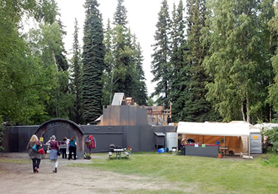 Photo of the people walking down a path toward a theater stockade, concession tent to one side, trees in the background