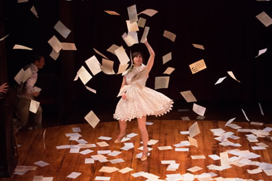Sylvia in a thigh-high, billowing white dress with papers falling all around her.