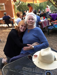 Photo of Willow Geer leaning on Ellen Geer's shoulder sitting at an outdoor table