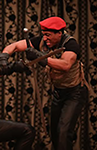 HenryIV-Powell K.P. Powell as Hotspur in Henry IV, Part One, wearing a red cap, olive green and black t-shirt, and black pants weilding a sword