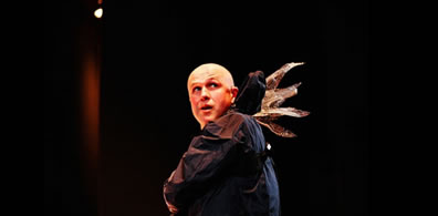 A man, bald, with a rain slickeer and fairy wings coming from the base of the hood