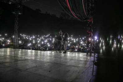 Photo from back stage of audiences on hill lighting up the stage