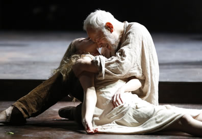 Lear in linen shit and brown pants cries with his forehead resting against the chin of Cordelia who lies dead in his arms, her body still dressed in the white slip
