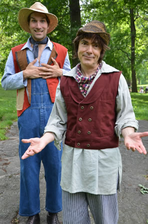 Corin in brown striped farmers hat, plaid scarf tied around neck, long linen shirt coming out below his double-breasted red vest, blue-striped pants with hands outstretched, behind him Silvius in straw hat, orange vest, blue shirt and blue overalls with hands to heart.