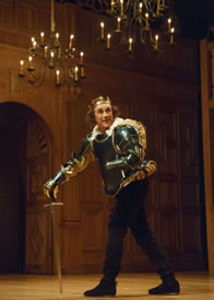 Richard in green armor, wearing crown, using his broadsword as crutch, with candle chandeliers hanging from the ceiling above