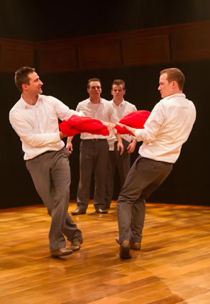 Two boys pulling on a red fabric circle each other as two other boys in the background watch, all in white shirts and tan trousers.