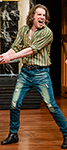 Shrew_O'Reilly-2 Aiden O'Reilly as Petruchio laughing in The Taming of Shrew in a vertically green striped work shirt and faded blue jeans