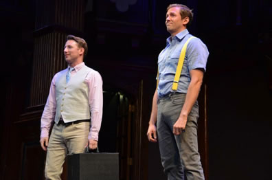 Valentine in pink oxford shirt, blue tie, tan vest and tan jeans holding a black suitcase in his left hand, Proteus in blue work shirt, gray jeans, and yellow suspenders