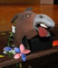 An ass's head, with tongue sticking out to one side, sits on the edge of a stage with construction paper flowers alongside.