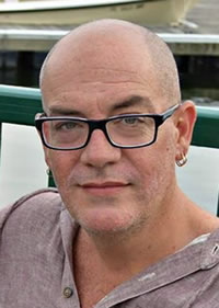 Head shot of Kevin Crawford, bald, wearing glasses, gray shirt