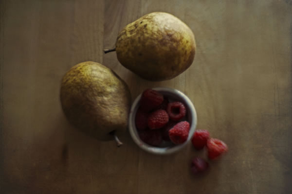 Two pears and a bowl of raspberries on a wood counter