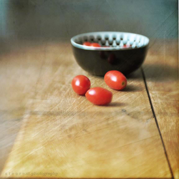 Three cherry tomatoes on countertop outside a bowl with others