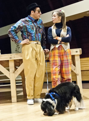 Launce and Speed stand against a platform, he in multi-blue-colored shirt and baggy gold pants, she in orange checkered pants, blue shirt and vest, with Crap grazing in front of them