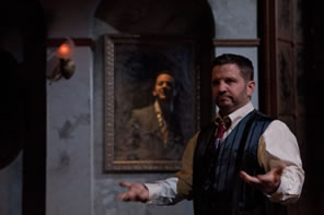 Richard in vest with hands out signing and in the mirror behind him Shadow in a suit