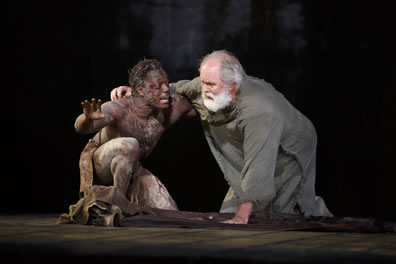 Edgar in only a loin cloth around his waist and hand up, kneels with Lear, in simple burlap-like rope, one hand on the groound,the other around Edgar's shoulder