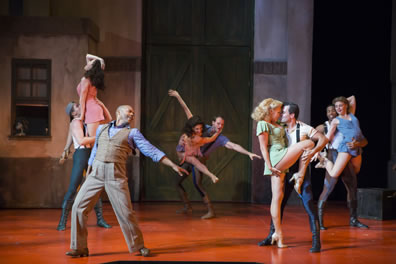 Dancers in various costumes dance in a backstage area.